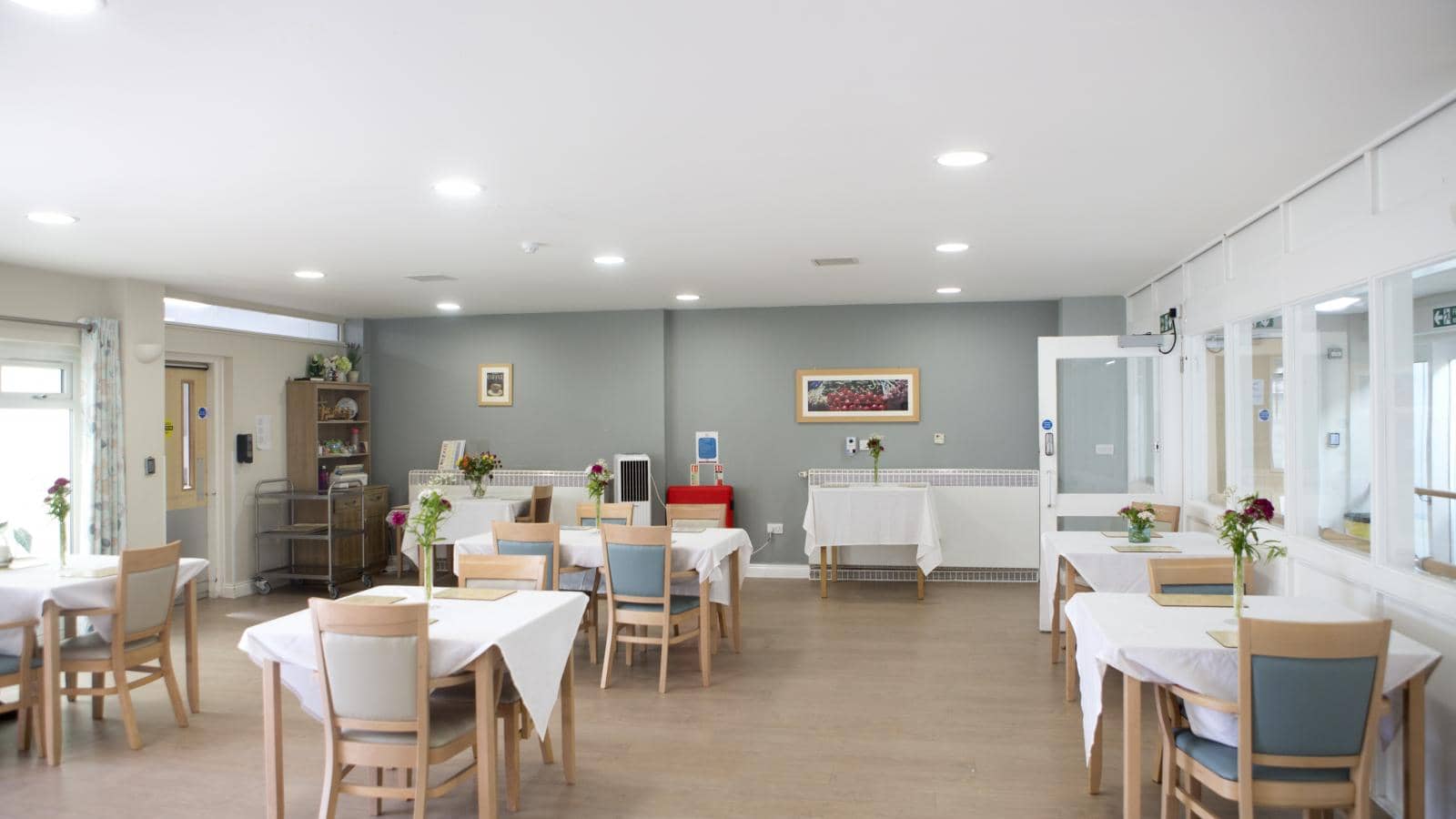 Communal and bright dining area of Kenbrook care home with multiple tables laid out ready to serve a meal