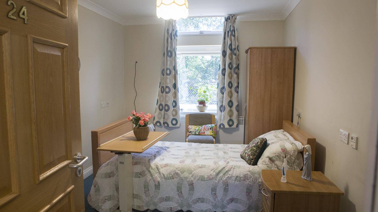 Bedroom with a double bed at Kenbrook care home with flowers on a table and view to outside space and trees