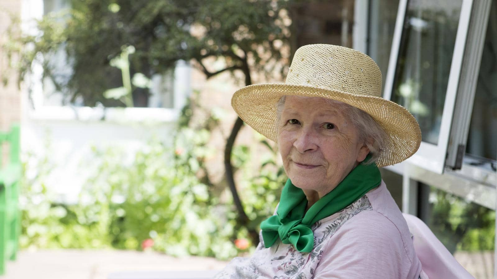 A care home resident sitting in the garden of Kenbrook care home wearing a sun hat smiling