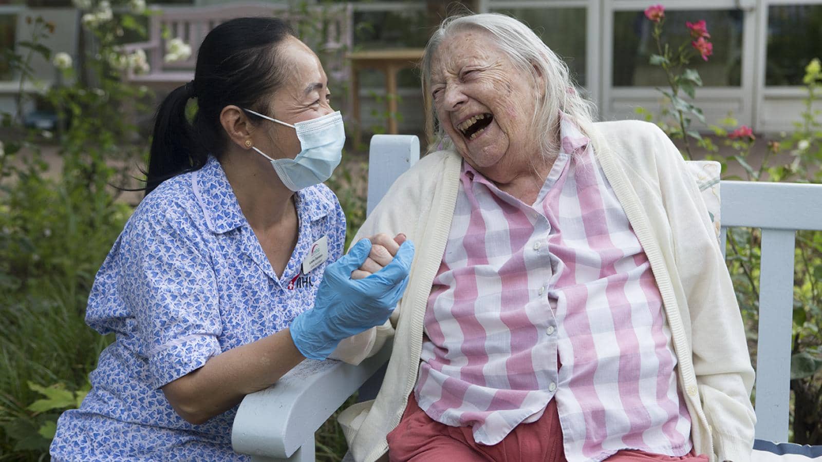 A female care home resident laughing outside with a care worker