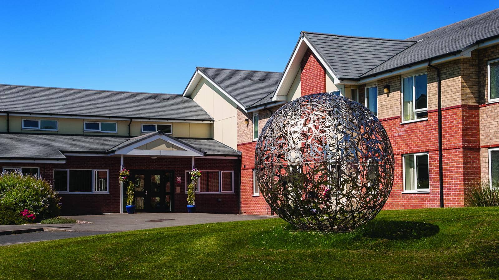 The entrance of Waterside House care home on a sunny day with a large metal circular sculpture