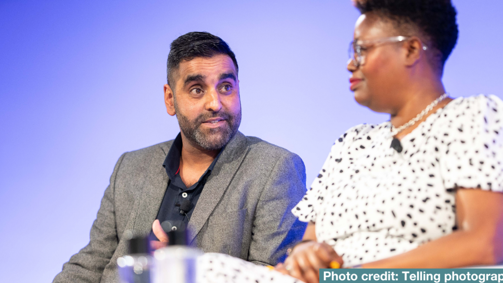 A man and woman are sat having a conversation at a panel event
