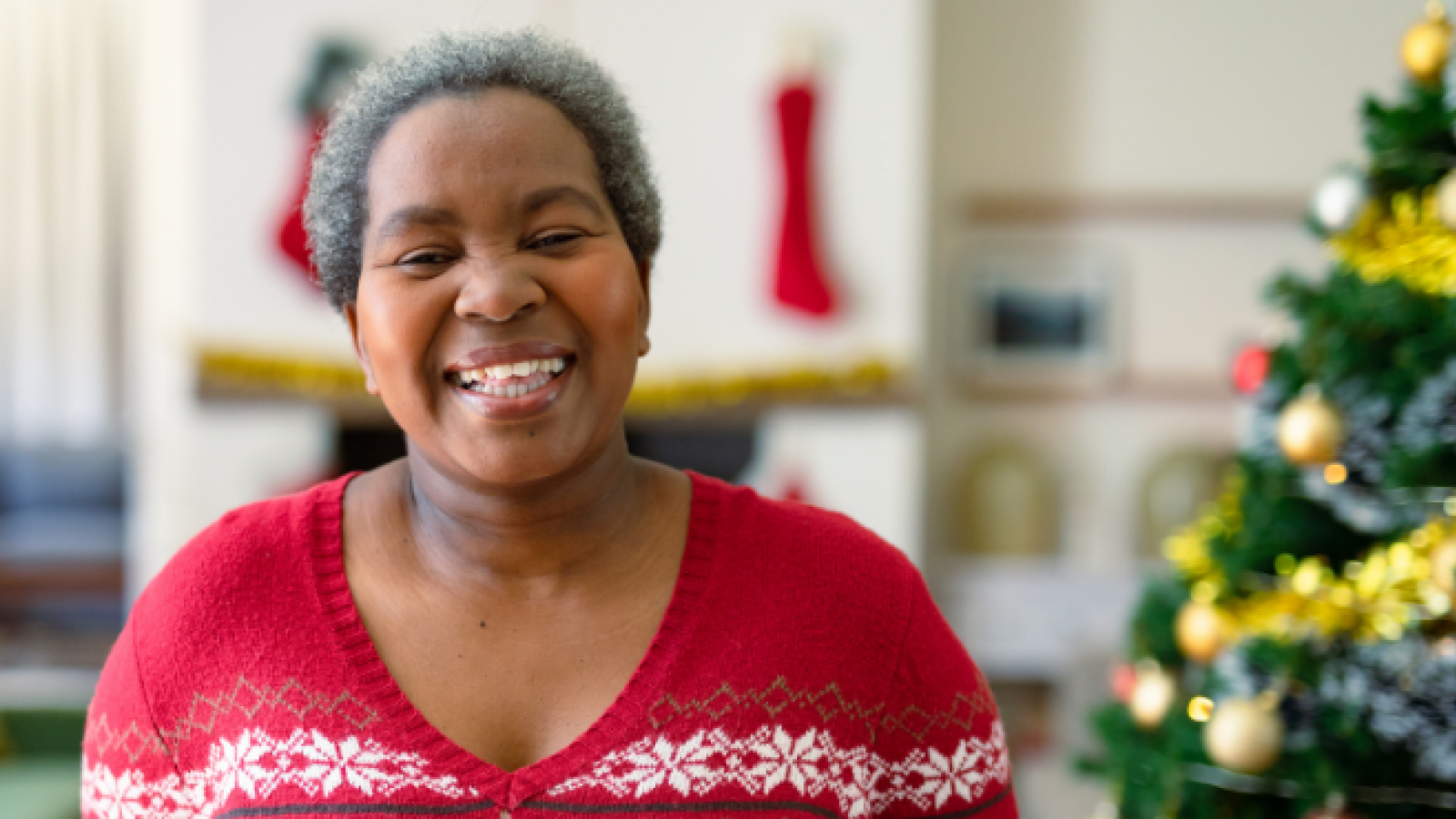 A lady is smiling stood in front of a Christmas tree