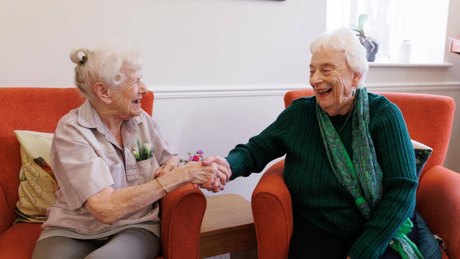 Two women are sat talking holding hands.