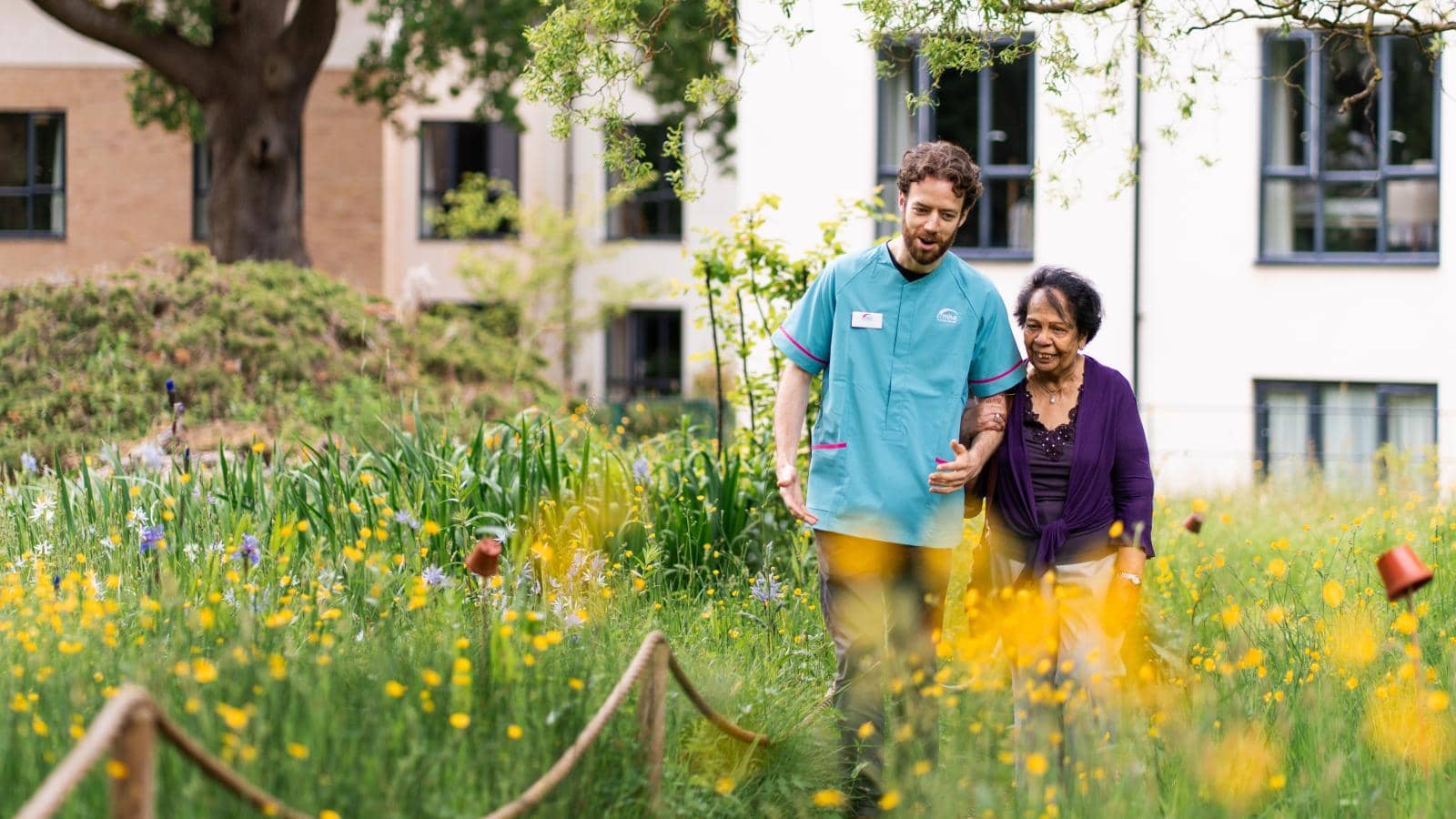 Male carer walking through care home garden with elderly lady