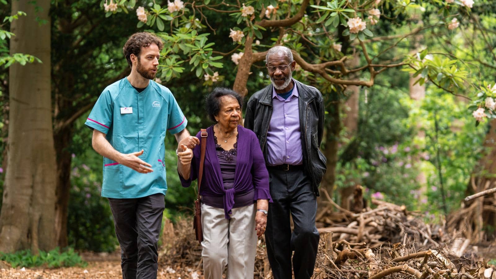 Male care assistant walking with an elderly couple outside