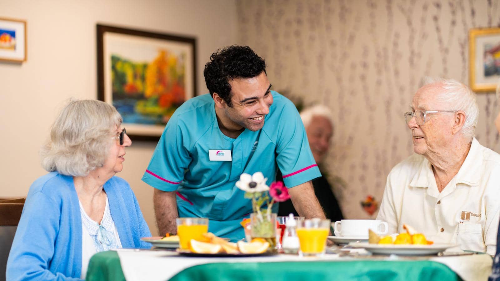 Older couple being served at a table by male care staff