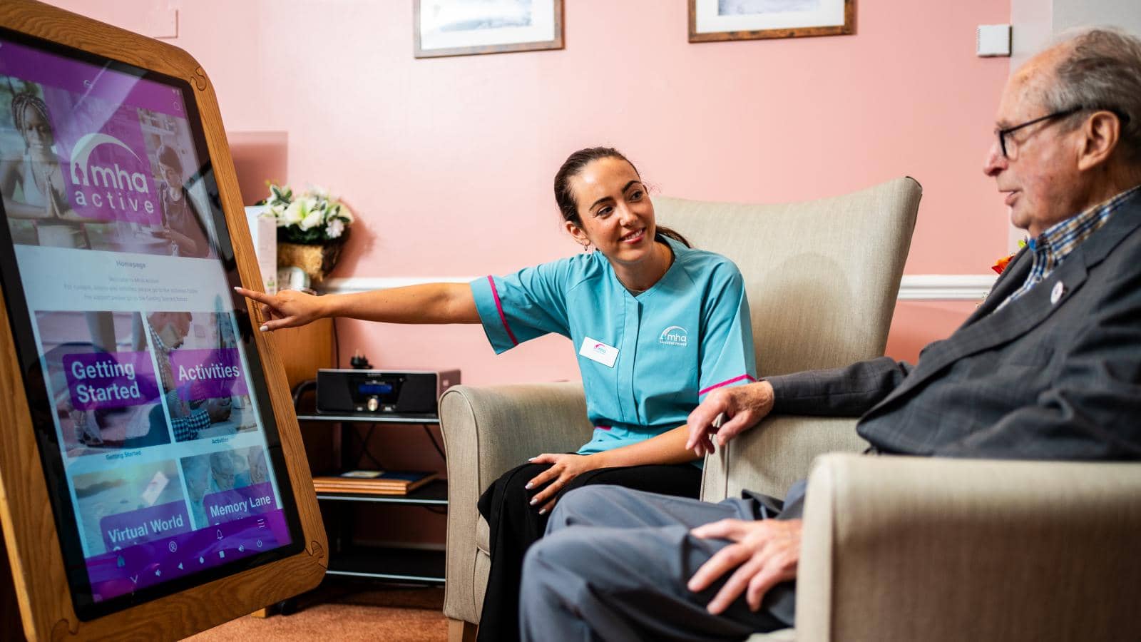 a caregiver interacting with an elderly man in a comfortable indoor setting using a tiny tablet