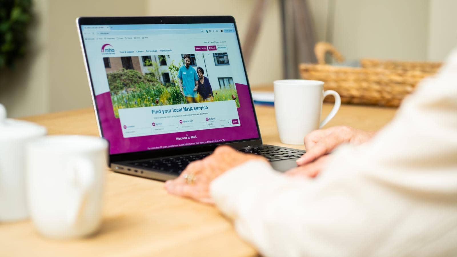 a person using a laptop on a wooden table whilst browsing the MHA website homepage