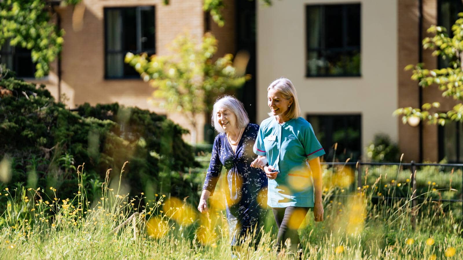 A resident and carer walking through the Wilderness, an extensive MHA garden area situated directly behind Hall Grange.