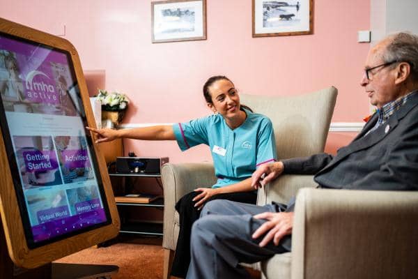 a caregiver interacting with an elderly man in a comfortable indoor setting using a tiny tablet