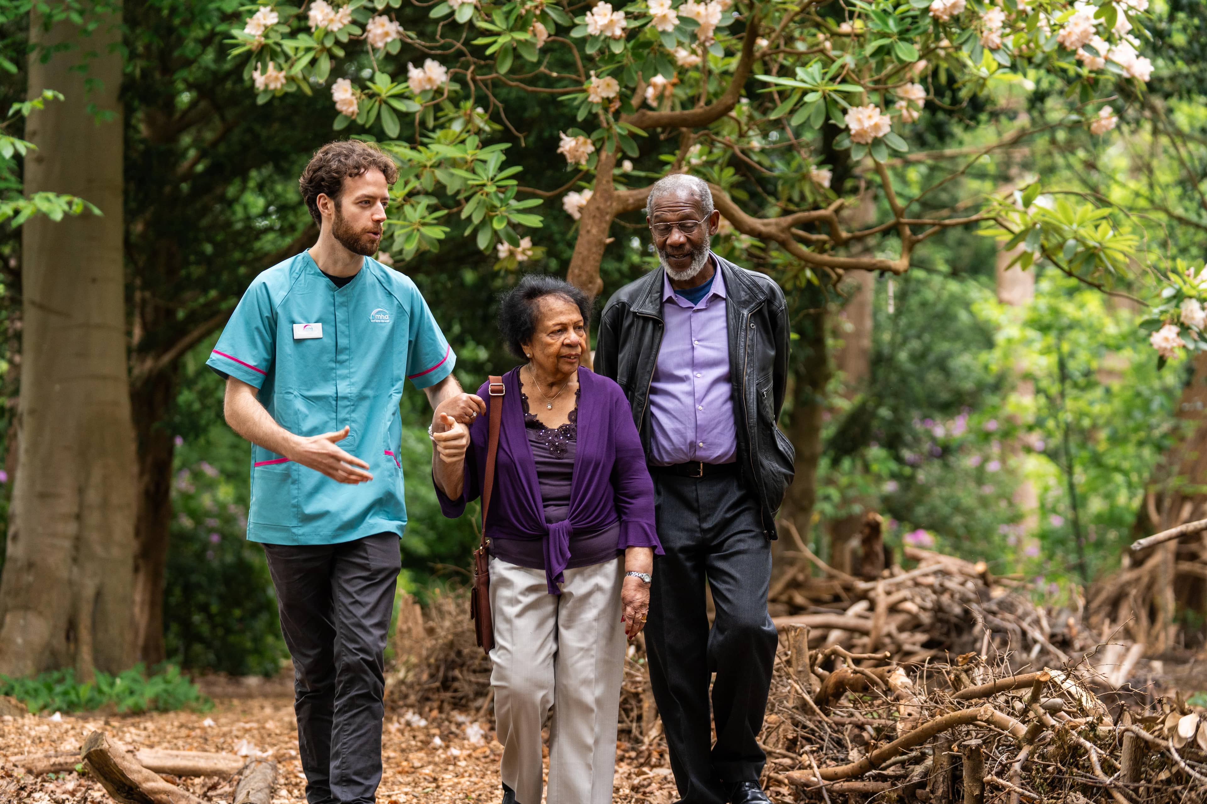 Male care assistant walking with an elderly couple outside