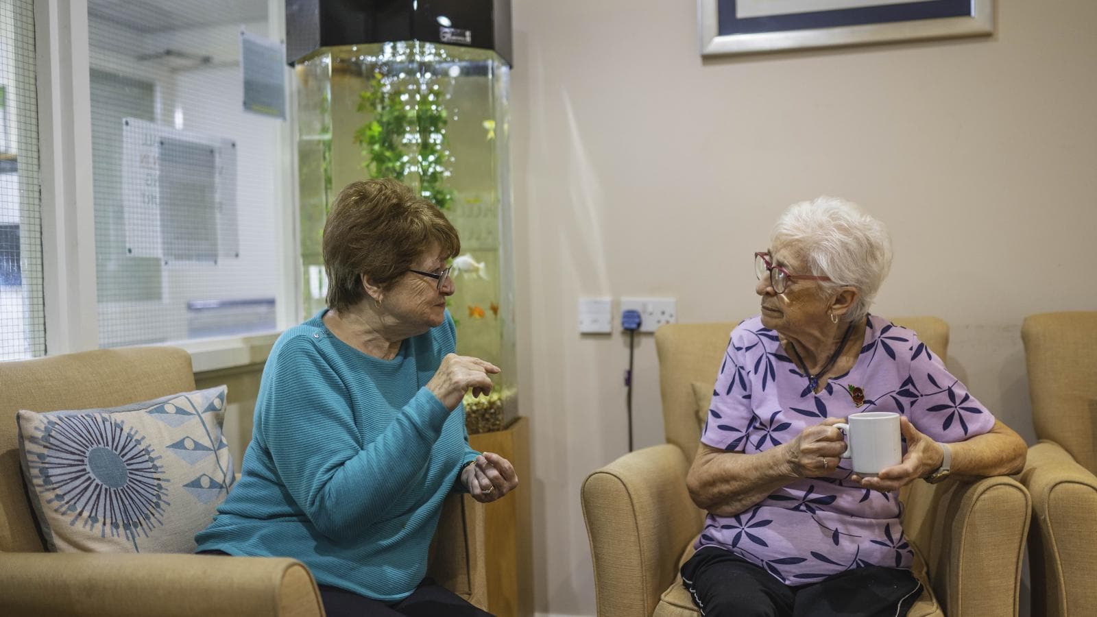 Two retirement living residents sit in the lounge having a chat 