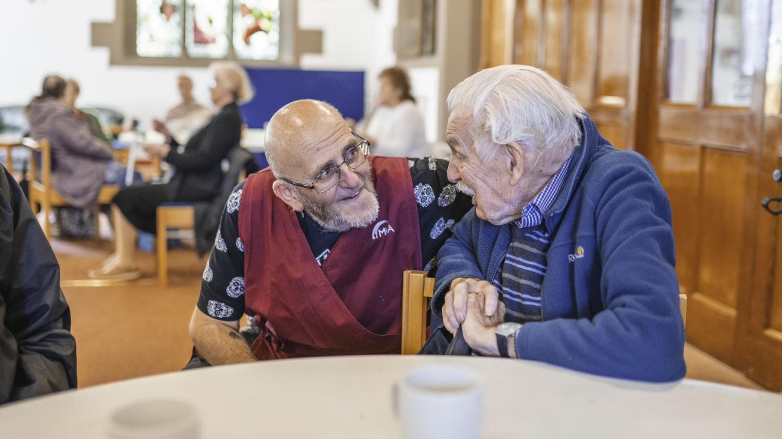 A male volunteer speaks to an older man at a community group. 