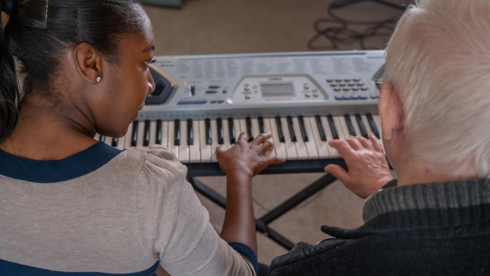 A music therapist sits at a keyboard with a resident 
