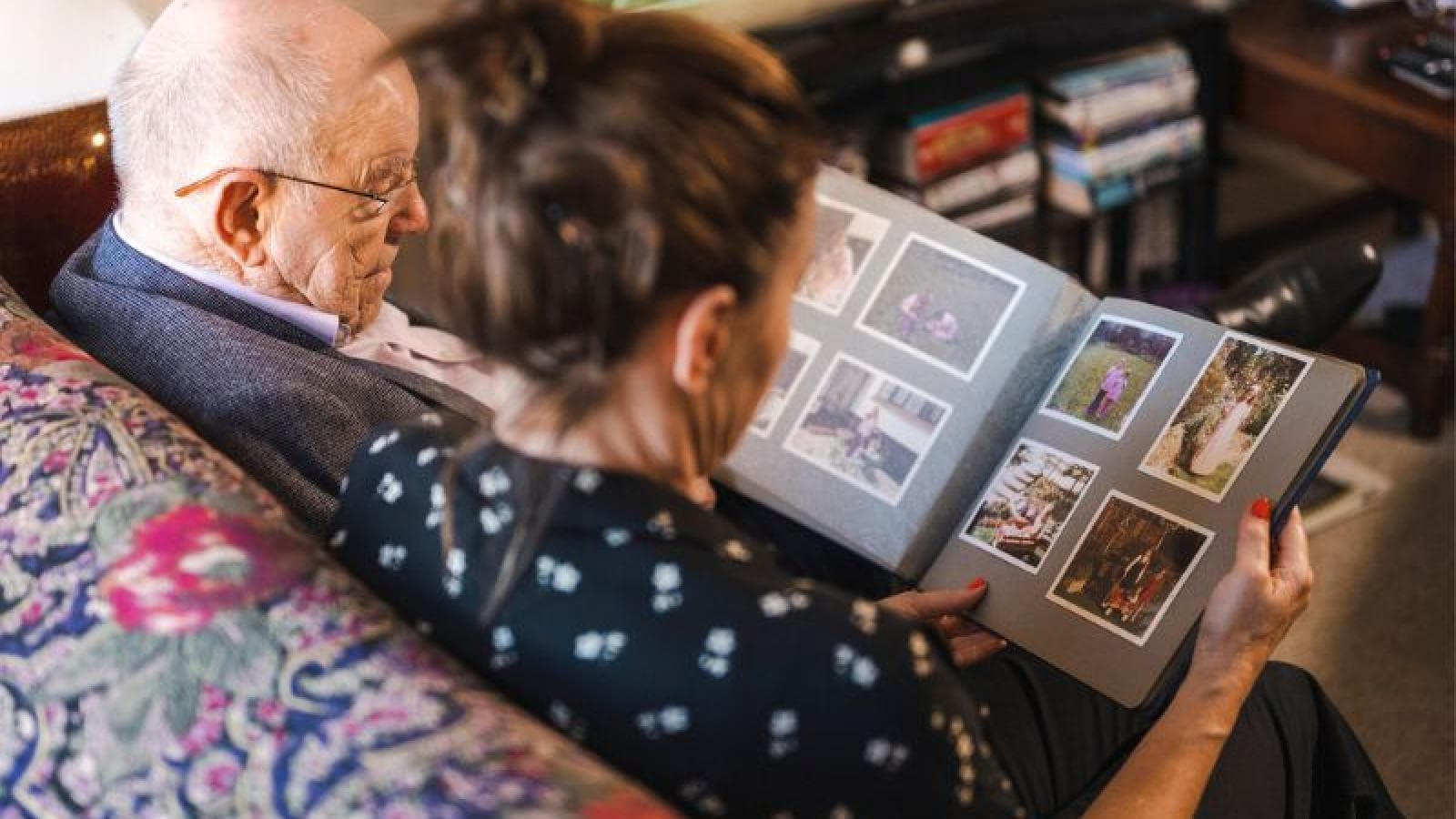 Two people sit together looking through a photo album. 