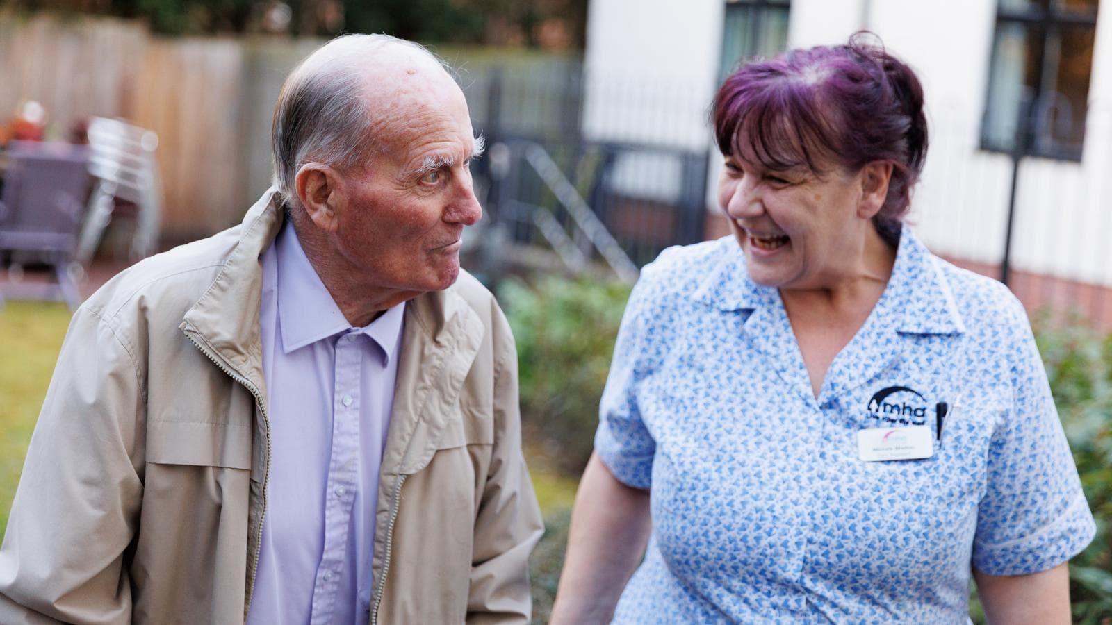 Care assistant laughs with a male resident outside in the garden