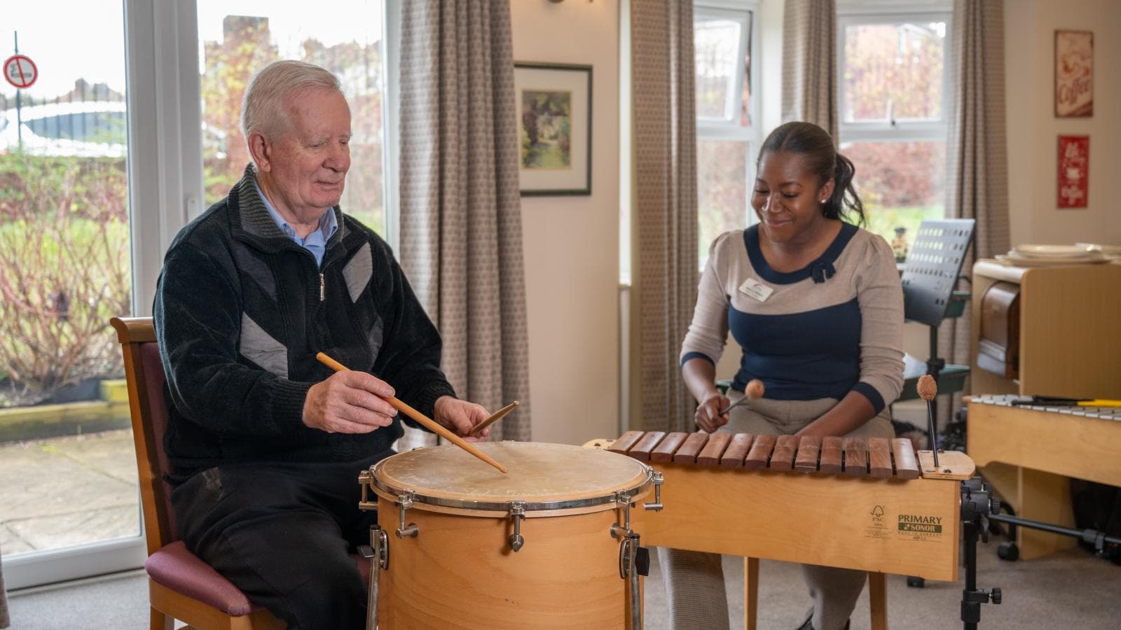 Male resident plays drums whilst music therapist plays xylophone