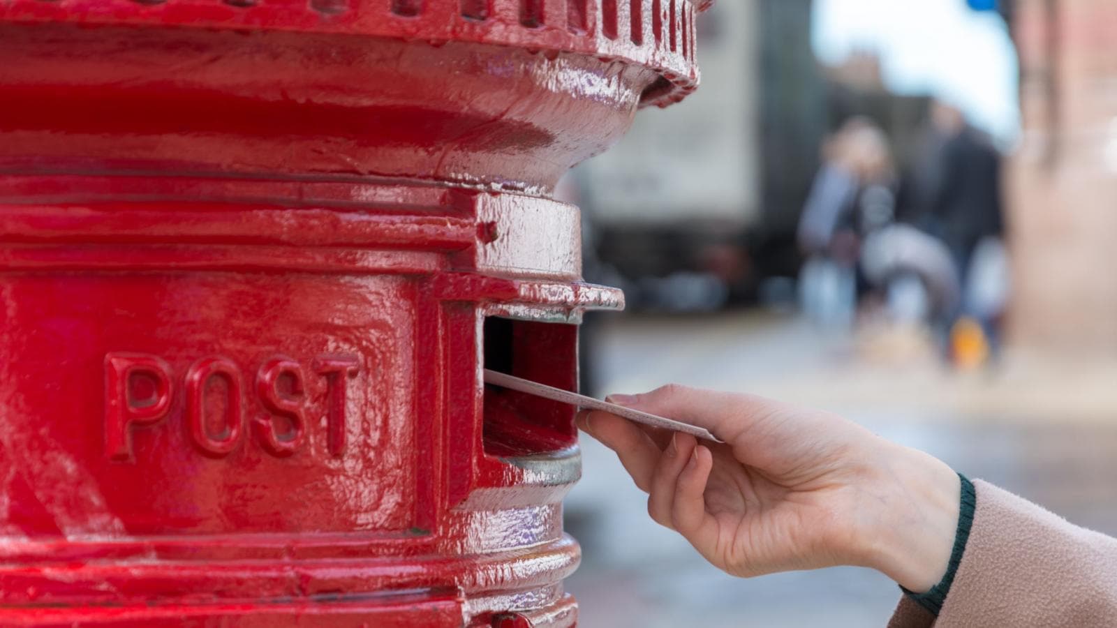 Person posting a letter in red postbox