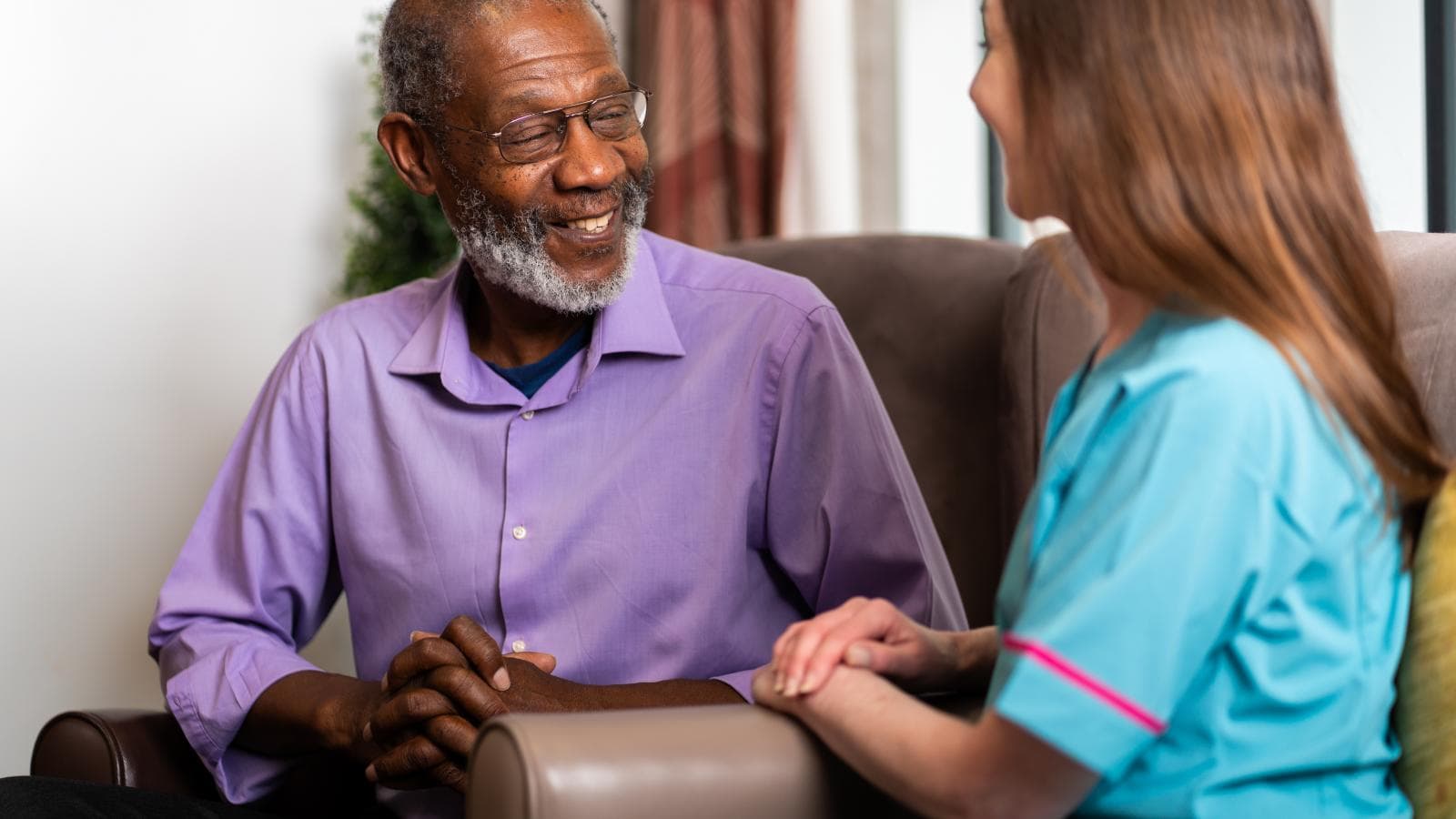 Male wearing pink shirt with grey hair speaking to female care assistant