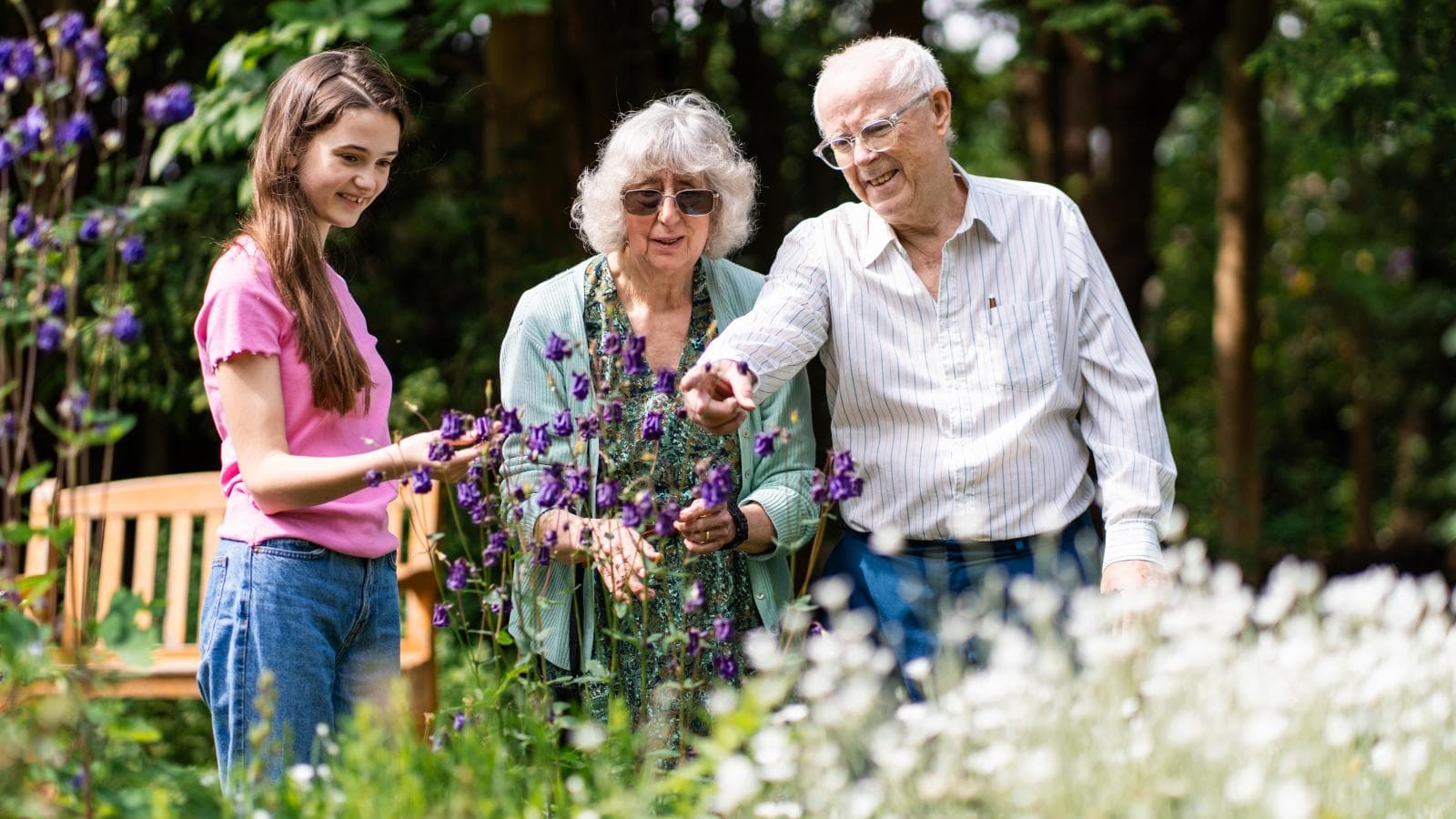 Grandparents pointing at flowers in garden with young granddaughter