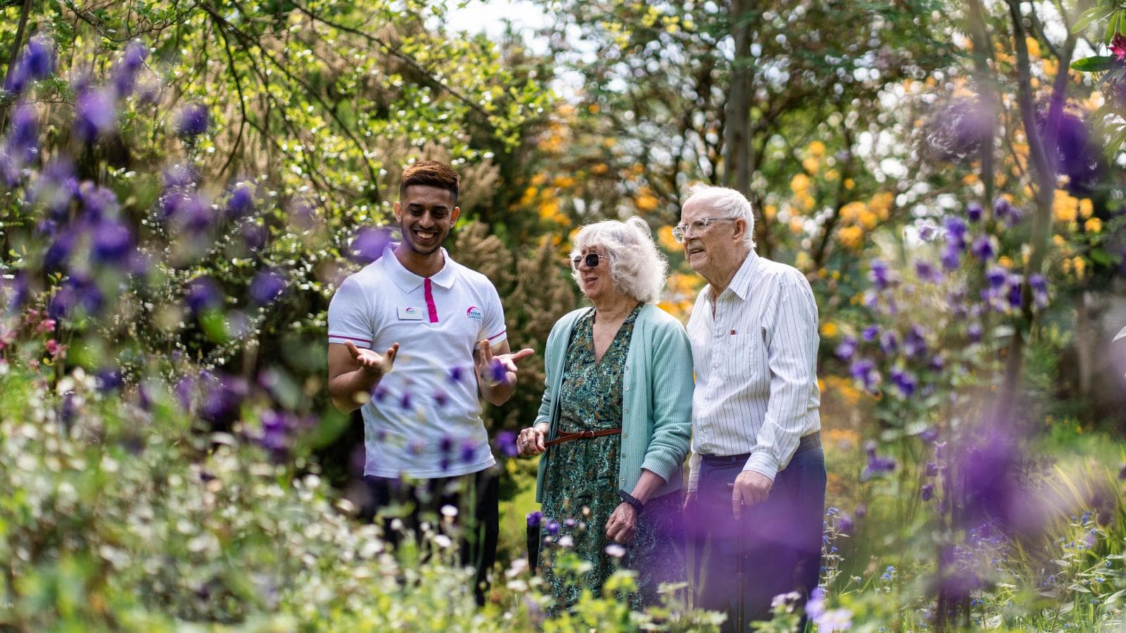 Elderly couple stood with younger man in a garden looking at the flowers together