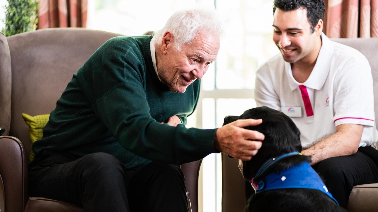 Man with grey hair stroking a black Labrador dog with male activities co-ordinator