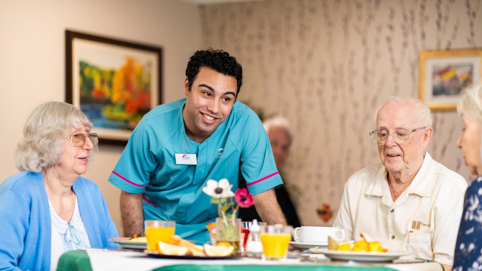 Male care assistant supporting care home residents during mealtime
