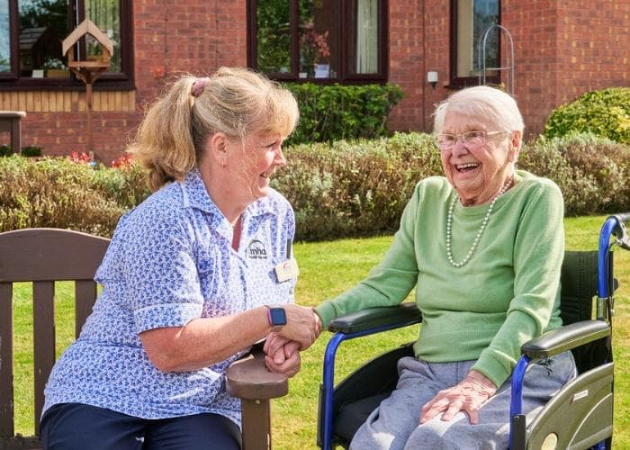 A carer holds the hand of a female resident sitting in a wheelchair in the garden