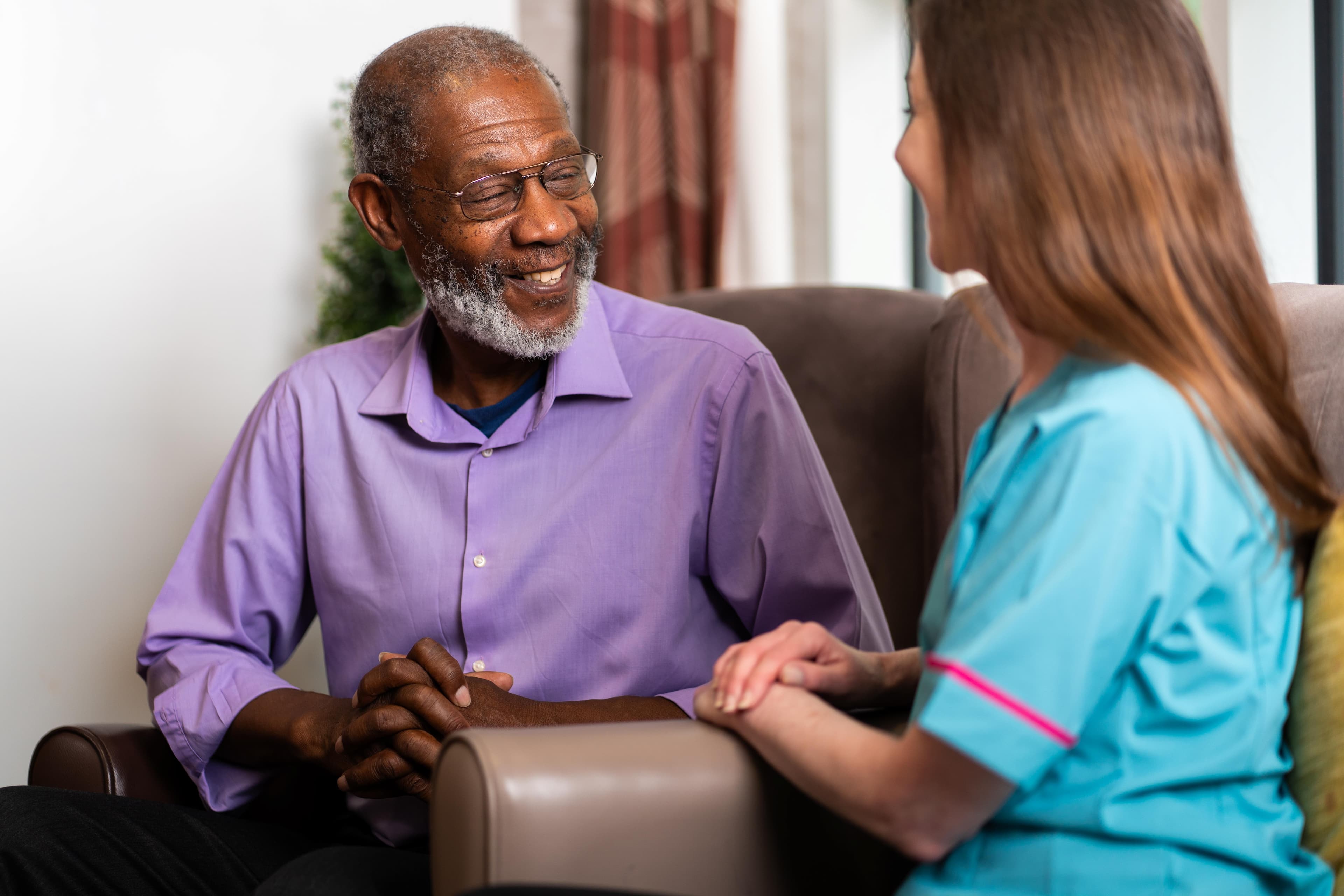 Male wearing pink shirt with grey hair speaking to female care assistant