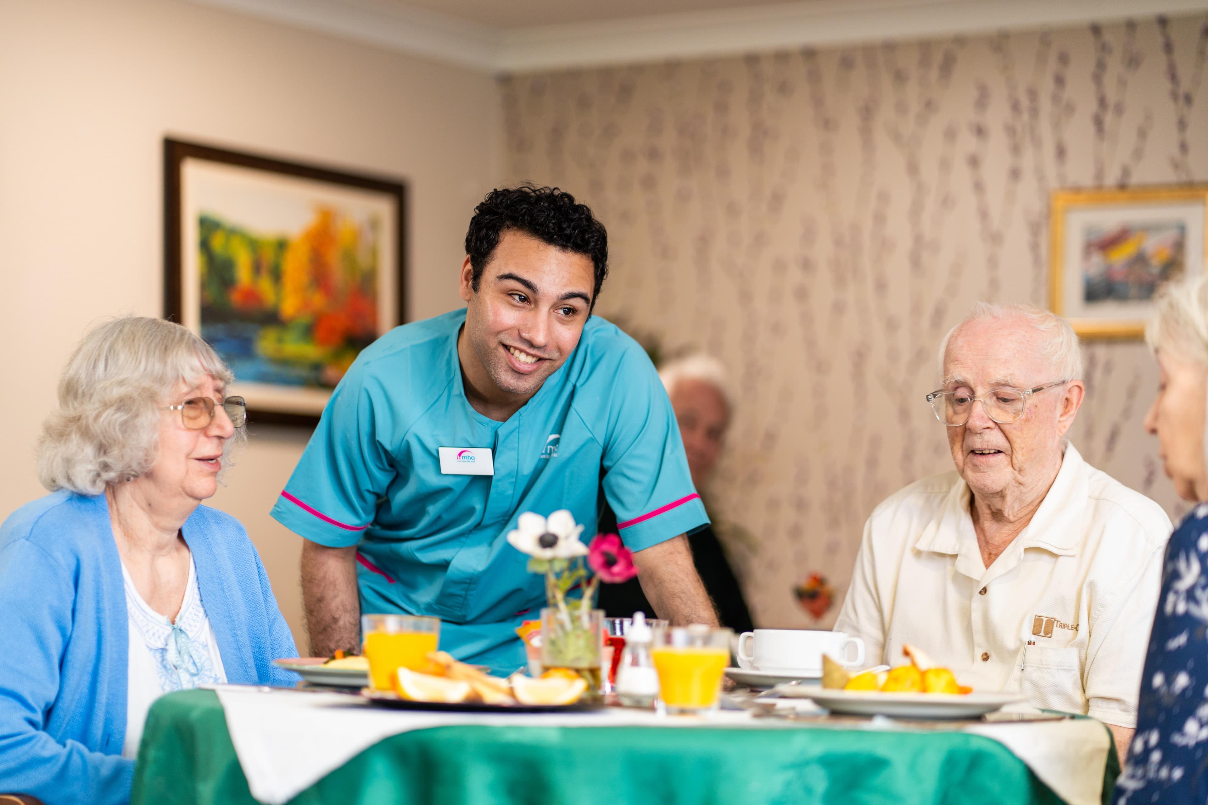 Male care assistant supporting care home residents during mealtime